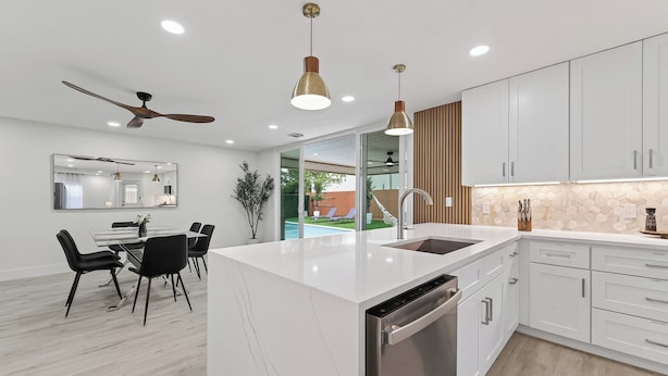 A modern kitchen with white cabinetry, a central island, and a dining area with black chairs. - Casa Esmeralda -Heated Pool, Luxury BBQ & Patio (Houston)