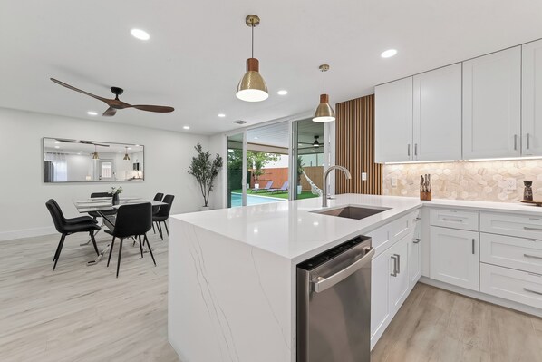 A modern kitchen with white cabinetry, a central island, and a dining area with black chairs. - Casa Esmeralda -Heated Pool, Luxury BBQ & Patio (Houston)