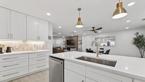 A modern kitchen with white cabinetry, a stainless steel dishwasher, a large island with a sink, pendant lighting, and a ceiling fan. - Casa Esmeralda -Heated Pool, Luxury BBQ & Patio (Houston)