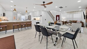 A modern kitchen with a central island, a dining area with a glass table, and a living space with a sofa and patterned cushions. - Casa Esmeralda -Heated Pool, Luxury BBQ & Patio (Houston)