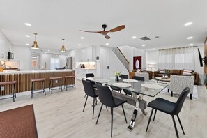 A modern kitchen with a central island, a dining area with a glass table, and a living space with a sofa and patterned cushions. - Casa Esmeralda -Heated Pool, Luxury BBQ & Patio (Houston)