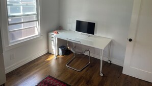 Una scrivania bianca con un monitor per computer, un cestino e una sedia trasparente.