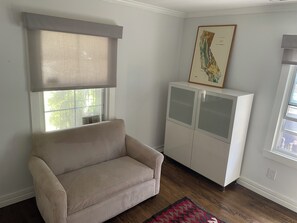 Ein Wohnzimmer mit einem beigen Sofa, einer Kommode, einem Fenster mit Jalousie und einer an der Wand hängenden Karte.