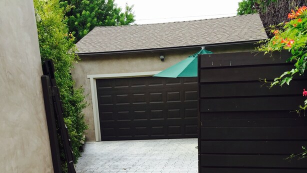 Una strada asfaltata che porta a un garage con cancello nero e tenda da sole verde.