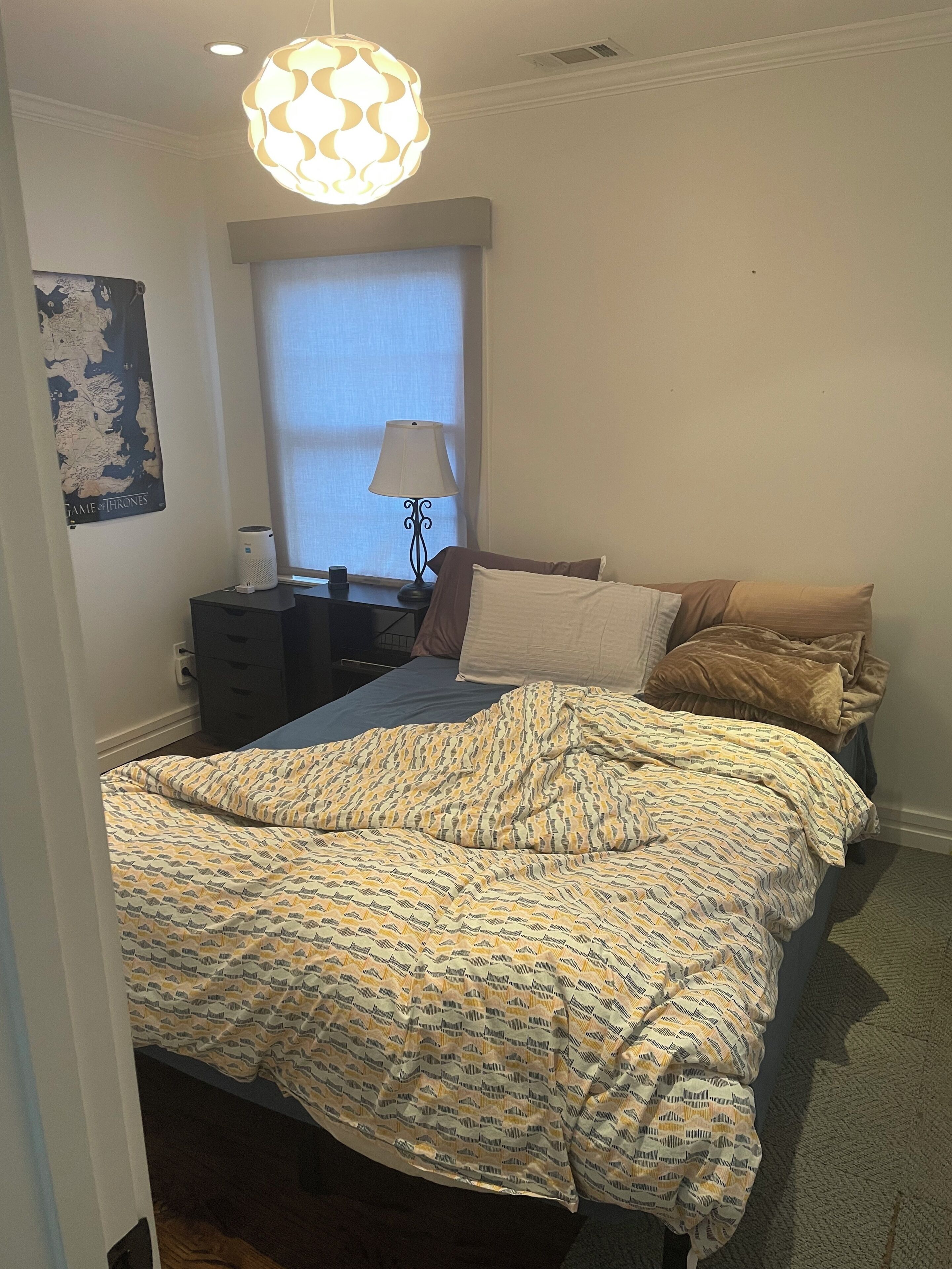 A bedroom with a bed, a lamp, a map on the wall, and a window.
