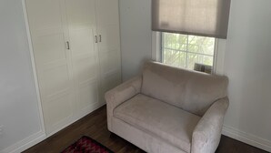 Una stanza con un divano beige, un armadio bianco e una finestra con persiana.