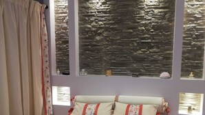 Ein Schlafzimmer mit Bett, Blumenmuster-Bettdecke, Vorhängen und einer Steinwand mit Fenstern.