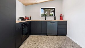 Ett kompakt kök med en inbyggd ugn, en diskmaskin och en liten arbetsbänk med en röd vattenkokare.