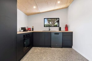 A compact kitchen with a built-in oven, a dishwasher, and a small countertop with a red kettle. - Matapouri Memories - 2 Houses! (Matapouri)
