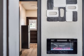 Un interior modern amb una llar de foc, una decoració mural geomètrica i una porta que condueix a una altra habitació.