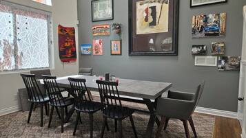 A dining area with a gray table and black chairs, framed artwork on the wall, and a window with decorative blinds.