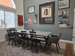 A dining area with a gray table and black chairs, framed artwork on the wall, and a window with decorative blinds. - Sunny and Spacious 5‑Bedroom San Diego Retreat - Walkable Near SDSU (San Diego)