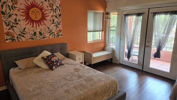 A bedroom with a bed, a nightstand, a bench, a window, and a sliding glass door.