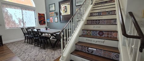 A staircase with motivational phrases, a dining area with chairs and a table, and a window with a view.