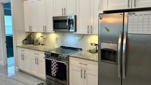 Una cocina moderna con armarios blancos, electrodomésticos de acero inoxidable, un reloj digital y un calendario en el refrigerador.