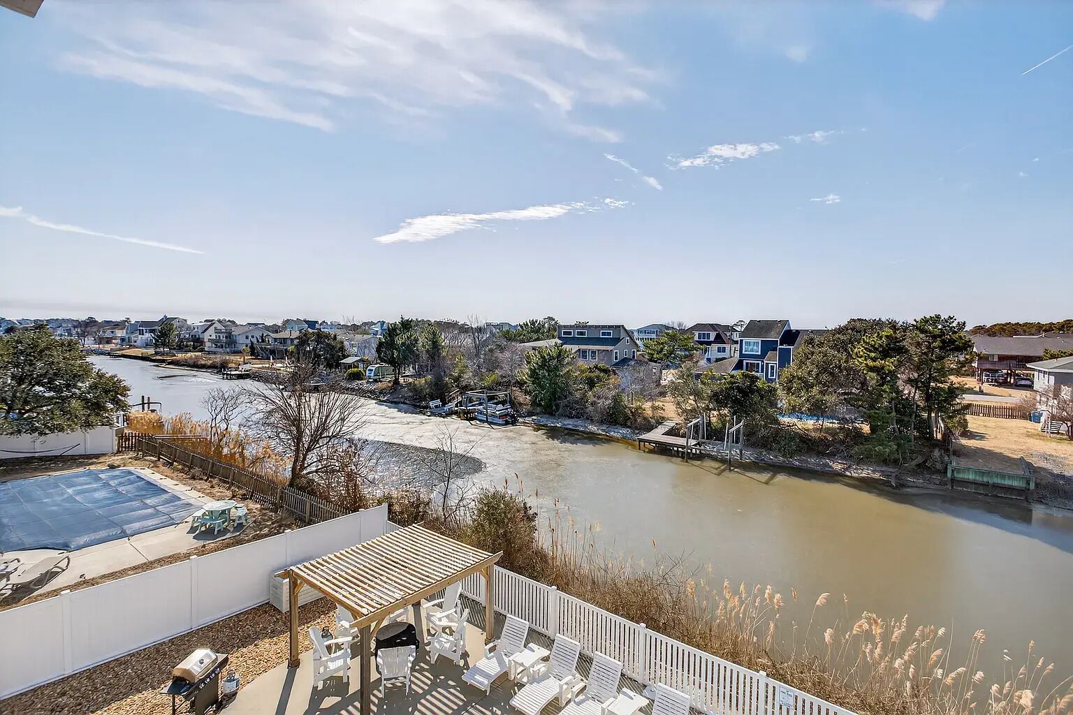 A riverside view with a patio area, outdoor seating, and a view of the river and surrounding houses.