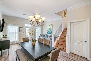 A dining area with a dark wooden table, cushioned chairs, a chandelier, and a staircase leading to another level. - 2 Side-by-Side Homes | 8BR, 2 Private Pools, Sleeps 28, Walk to Beach (Panama City)