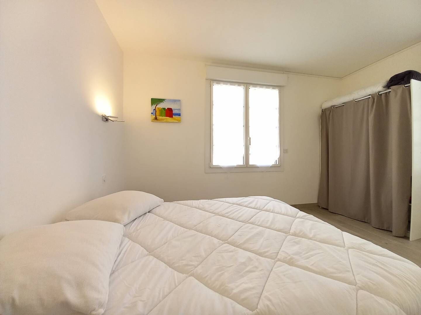 Une chambre à coucher avec un lit, une fenêtre, un rideau et un luminaire fixé au mur.