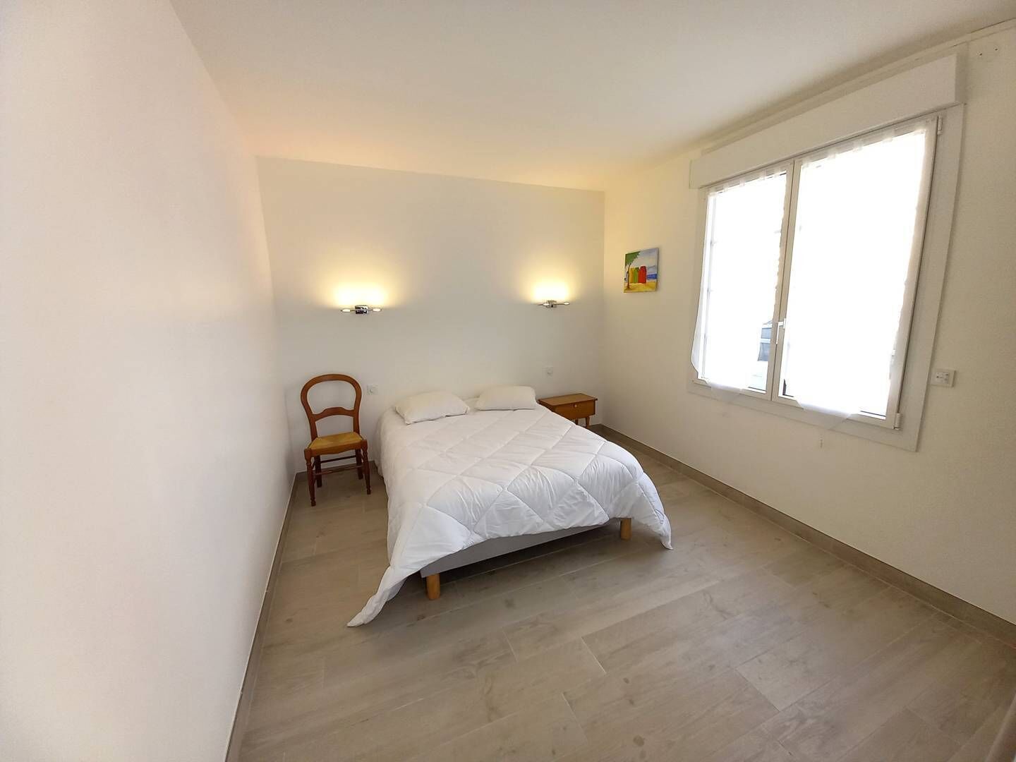 Un dormitorio con una cama, dos luces en la pared, una silla, una mesita y una ventana.