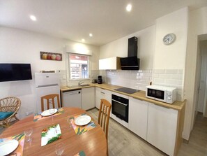 A compact kitchen with a microwave, stove, sink, and a clock on the wall. - Royan Center – BEACH  et  SHOPS WITHIN WALKING DISTANCE – GROUND FLOOR APARTMENT (ROYAN)