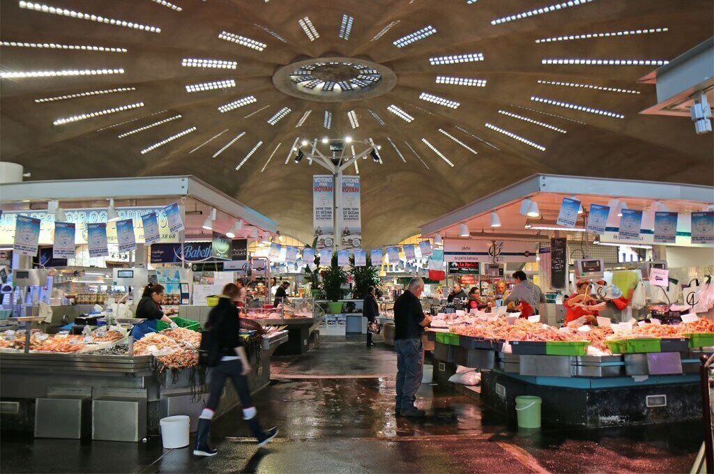 A bustling indoor market with multiple stalls selling seafood, under a modern ceiling with radial lighting.