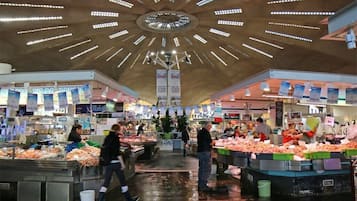 A bustling indoor market with multiple stalls selling seafood, under a modern ceiling with radial lighting.