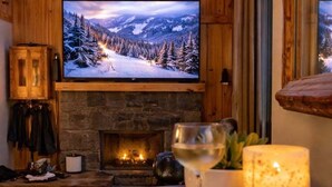 A cozy room with a fireplace, a television displaying a snowy landscape, and a glass of wine on the table. - Slopeside Lodge at Sugar Mountain - Ski In/Out, Views, Near Water, Gas Fireplace (Sugar Mountain)