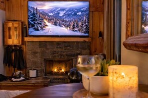 A cozy room with a fireplace, a television displaying a snowy landscape, and a glass of wine on the table. - Slopeside Lodge at Sugar Mountain - Ski In/Out, Views, Near Water, Gas Fireplace (Sugar Mountain)
