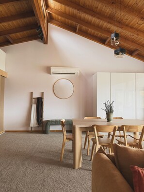 A dining area with a wooden table and chairs, a round mirror on the wall, a ceiling fan, and an air conditioning unit.
