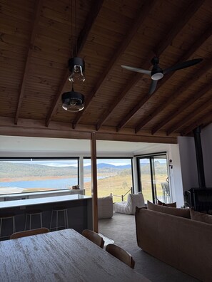 A modern interior with a wooden ceiling, large windows, a sofa, and a dining area.