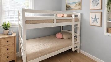 A bunk bed with a wooden frame, a bedside table with drawers, a small potted plant, and a wall with framed pictures.