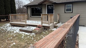 A small building with a porch, a fenced area, and a snow-covered ground.