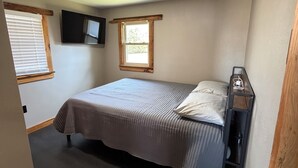A bedroom with a bed, a window, a mounted TV, and a ceiling light.