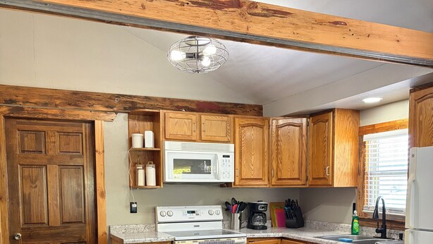A kitchen with wooden cabinets, a white refrigerator, a stove, a microwave, and a dining table with chairs.