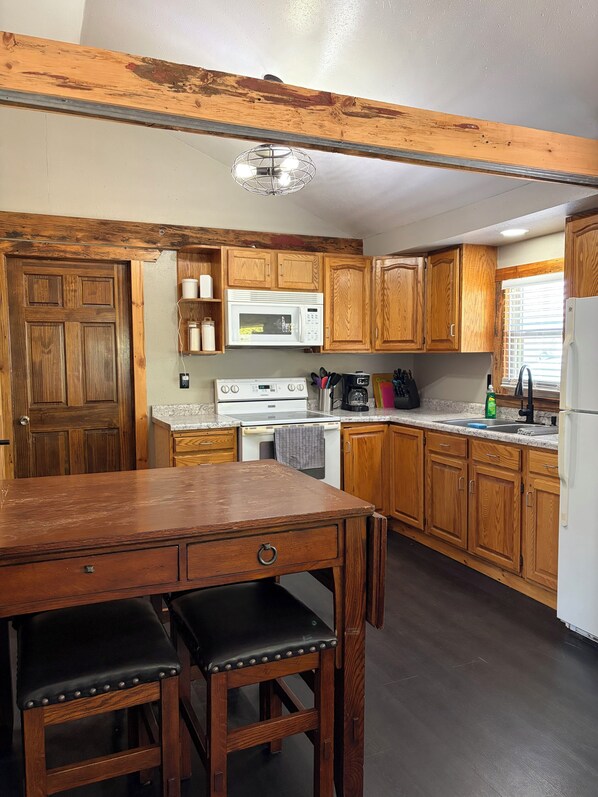 A kitchen with wooden cabinets, a white refrigerator, a stove, a microwave, and a dining table with chairs.