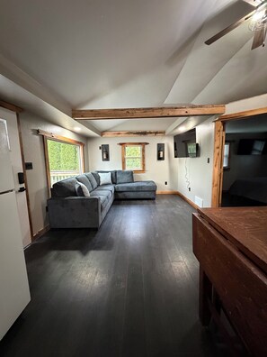A modern kitchen with dark wooden flooring, a grey sectional sofa, and a wooden dining table.
