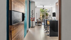 En modern inredning med en väggpanel i trä, en platt-TV, en matplats med stolar och ett bord samt en takfläkt.