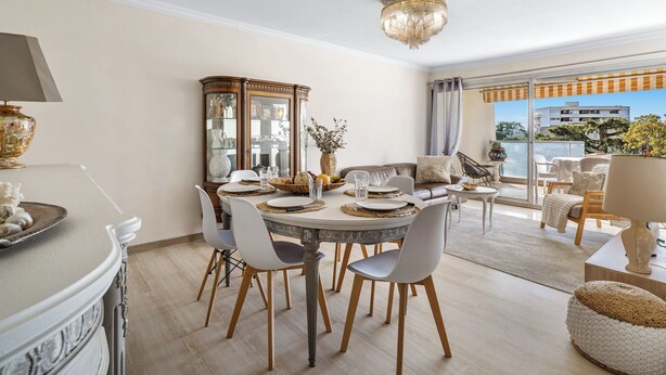 Un espace repas comprenant une table ronde, des chaises, un lustre et une vue sur l’extérieur, visible à travers une porte vitrée.