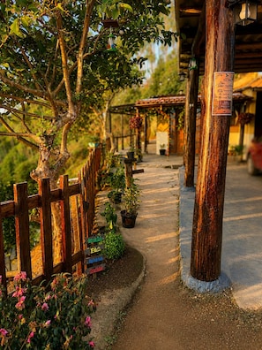A pathway leading to a rustic building with a wooden fence, potted plants, and a signpost indicating amenities.