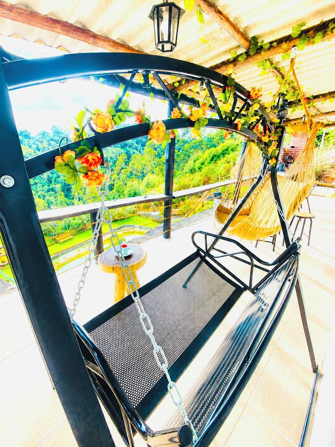 A metal swing chair with a mesh seat, a wooden table, and a hanging lantern.