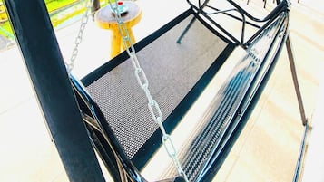 A metal swing chair with a mesh seat, a wooden table, and a hanging lantern.