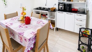 Une cuisine de taille réduite avec des meubles blancs, une cuisinière à gaz et un coin repas agrémenté d’une nappe à motifs floraux.