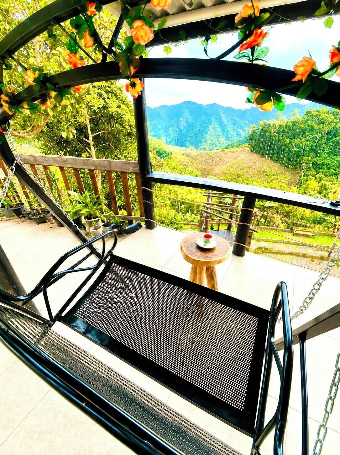 A balcony with a metal chair and table, surrounded by greenery and a view of mountains.