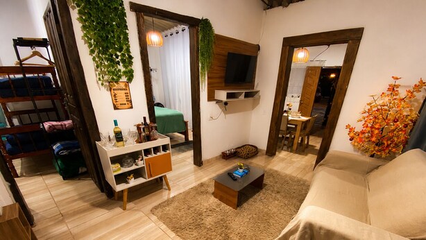 Un espace de vie compact comprenant un canapé, une table basse, un téléviseur fixé au mur, un petit meuble et une plante suspendue.