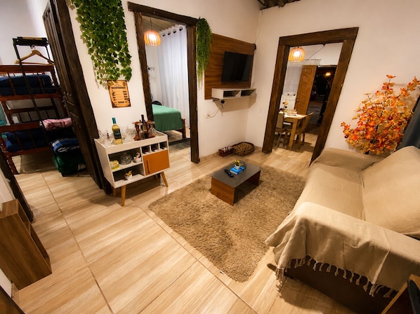 Un espace de vie compact comprenant un canapé, une table basse, un téléviseur fixé au mur, un petit meuble et une plante suspendue.