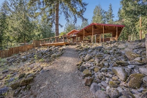 A wooden cabin with a red roof, surrounded by a forest and a rocky path leading to it. - Howard's Hideaway Riverfront Pet Friendly Cabin (Sandy)