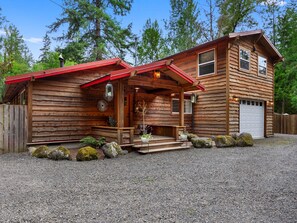 Eine Holzhütte mit Veranda, Garage und gepflasterter Auffahrt.