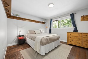 Ein Schlafzimmer mit Bett, Nachttisch, Schminktisch und einem Fenster mit Vorhängen.