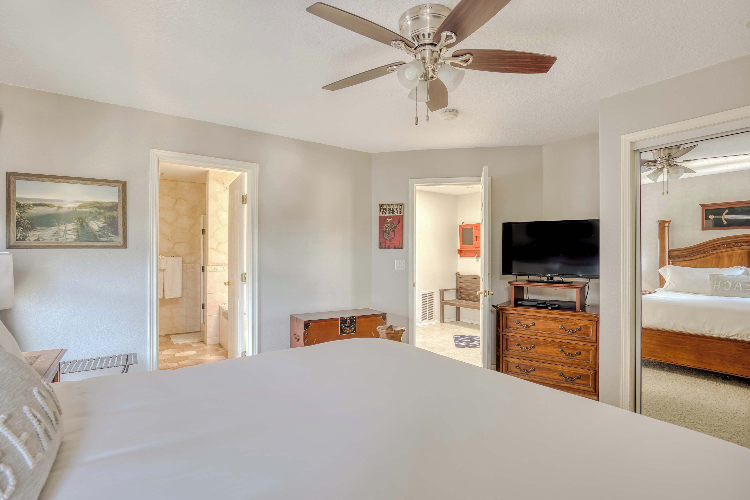 A bedroom with a bed, a television, a dresser, and a ceiling fan.