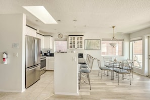 A modern kitchen with stainless steel appliances, a dining area with metal chairs, and a large window providing natural light.